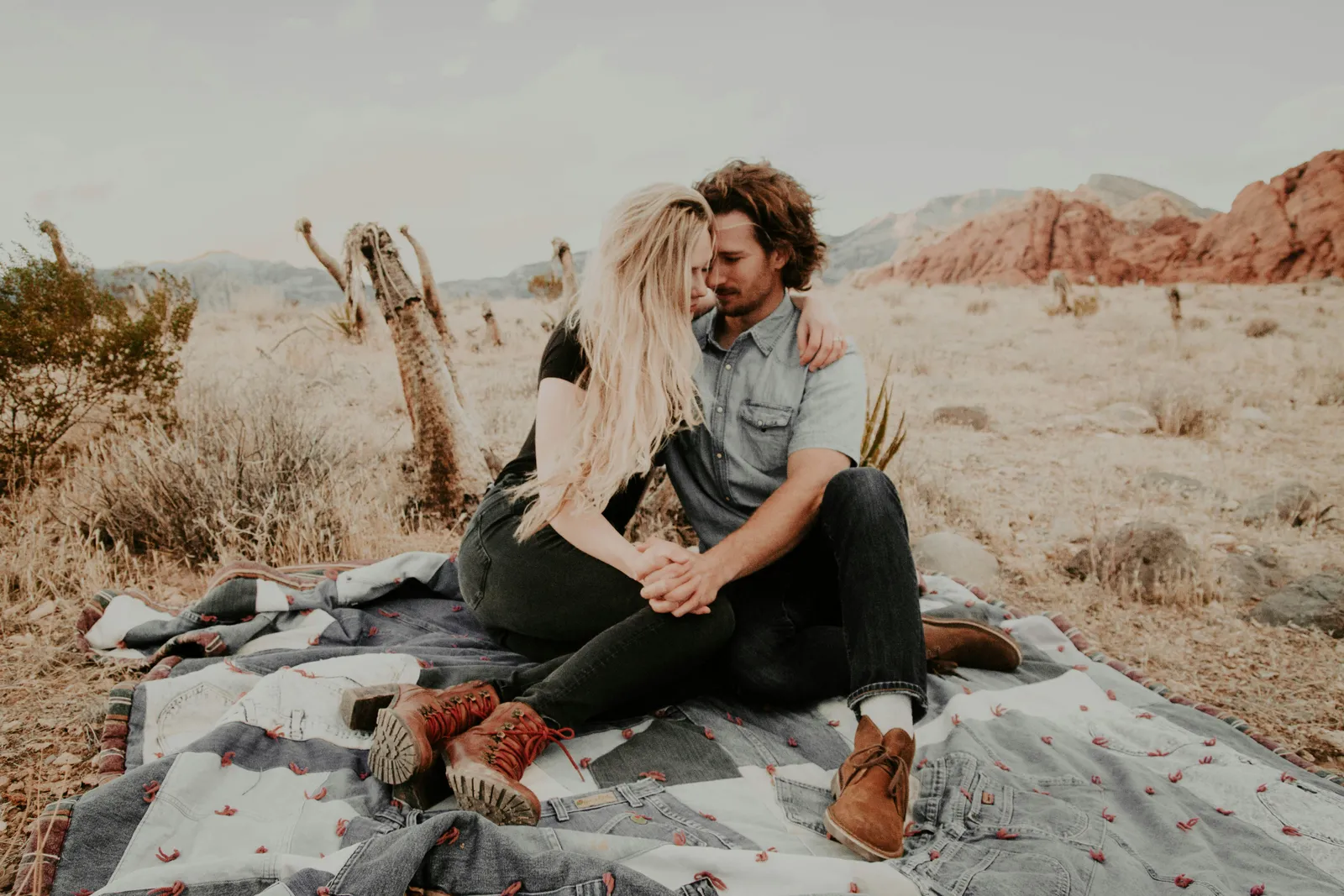 Couple sitting together on a blanket in a red rock desert landscape with cacti in the background.