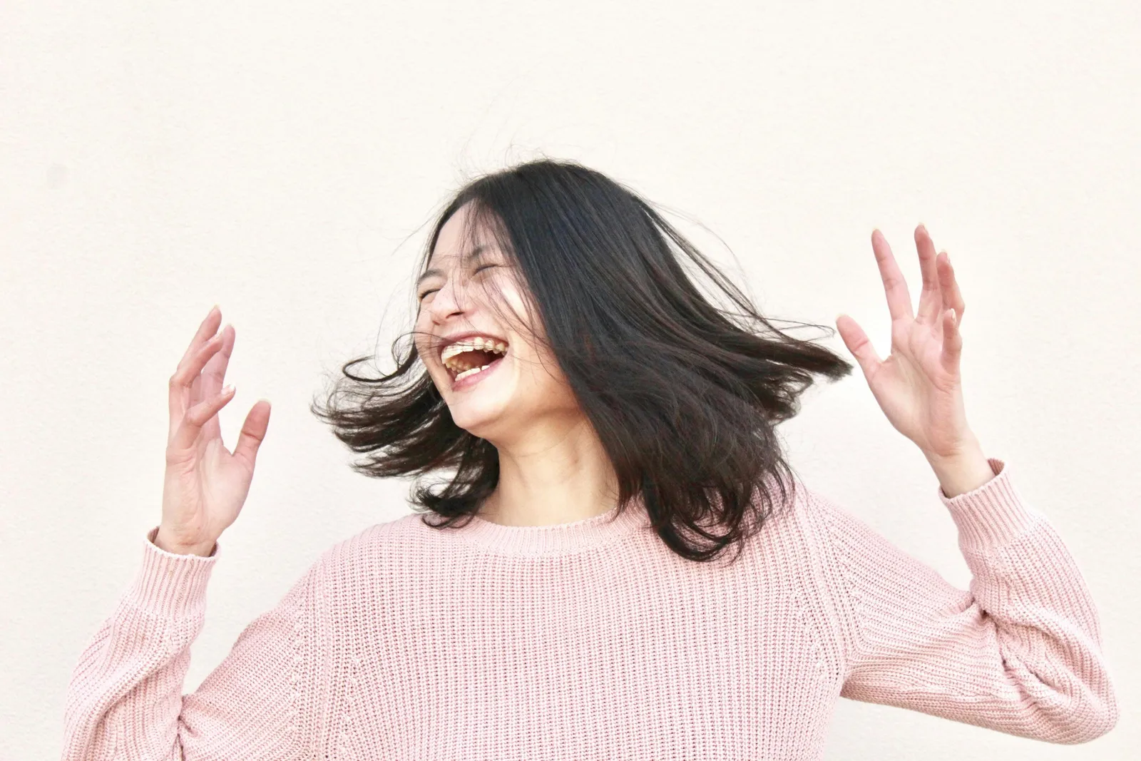 Young woman laughing with eyes closed and hands raised, joyful candid portrait against white background