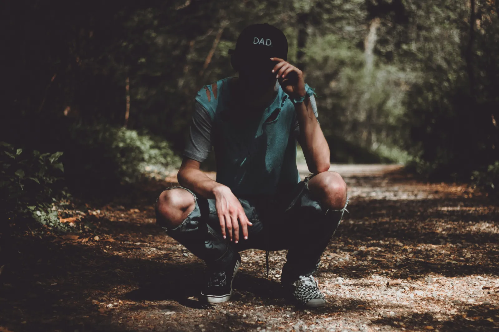 Young man crouching on a forest path, head down with hand covering his face