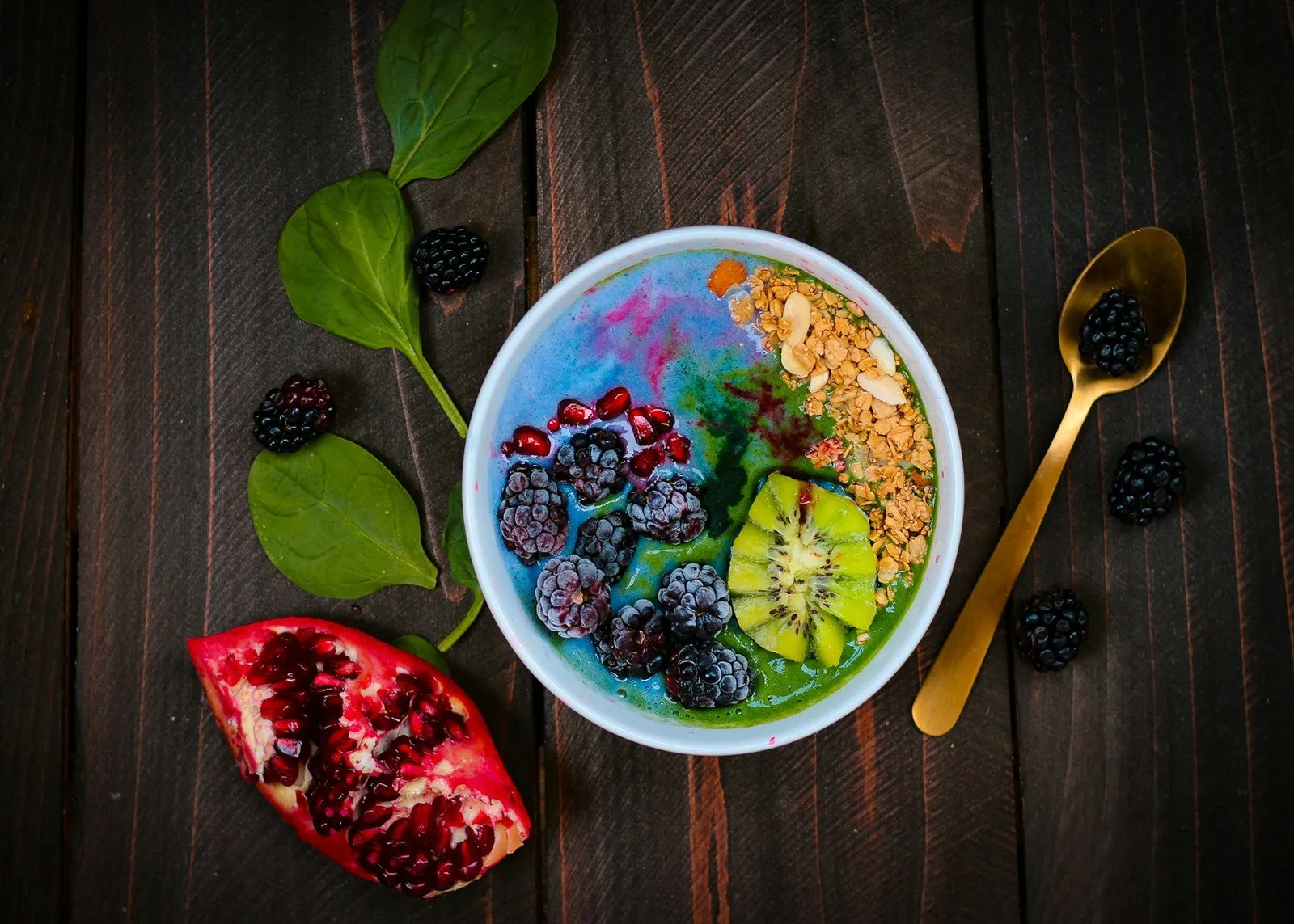 A breakfast bowl of layered acai, berries and granola on dark wood with a gold spoon, typical of the nutrient-dense, portion-controlled meals at most weight loss retreats.