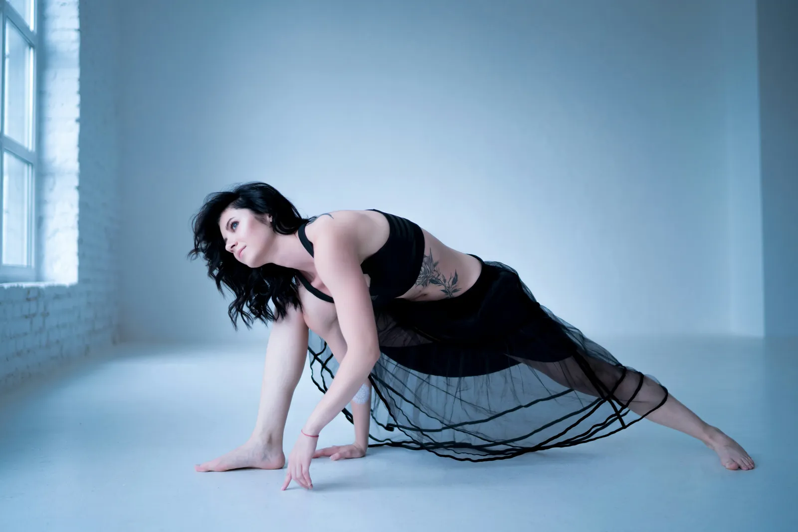 Woman in a low lunge pose in a bright minimalist studio with white walls. Accessible, foundational movement in a calm space.